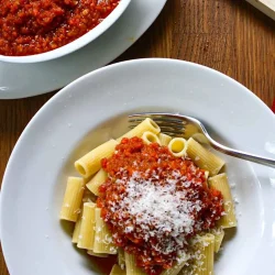 Un plato de pasta con rigatoni y falsa salsa boloñesa servido con queso parmesano, con un tenedor, todo sobre una superficie de madera.