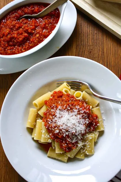 A bowl of rigatoni dressed with fake Bolognese sauce and Parmesan cheese, on a wooden surface.