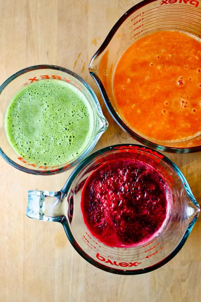  three glass measuring cups with carrot, cilantro and beet juice.