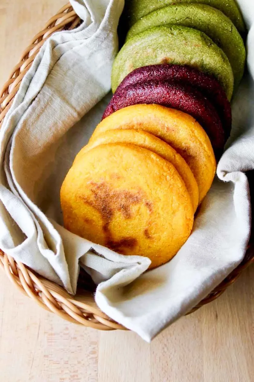 8 arepas mulcolores de vegetales en una toalla de lino beige dentro de una cesta