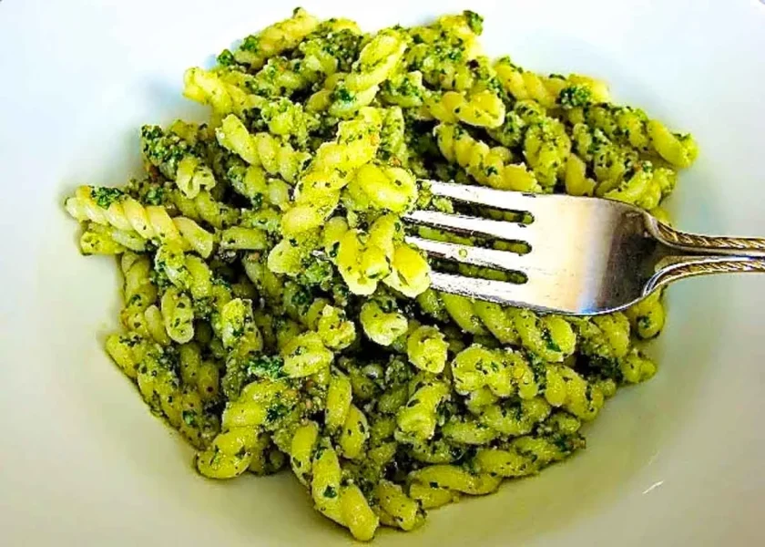 a fork with a a bite of pasta with arugula and walnut pesto.