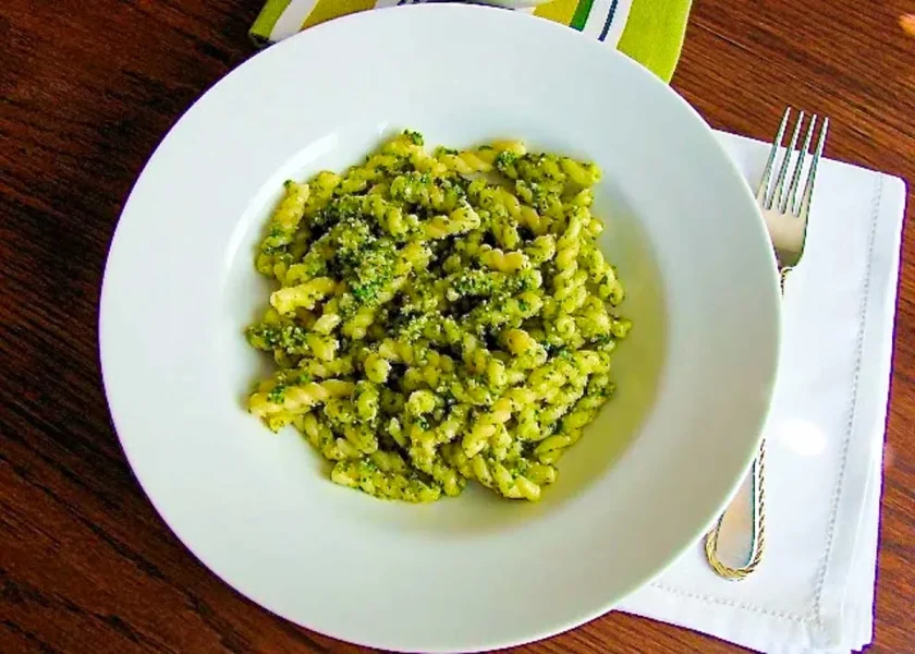 A white bowl with pasta with arugula and walnut pesto
