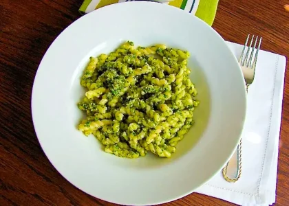 Un plato de pasta al pesto de rúcula y nueces, con una sercvilleta blanca y un tenedor.