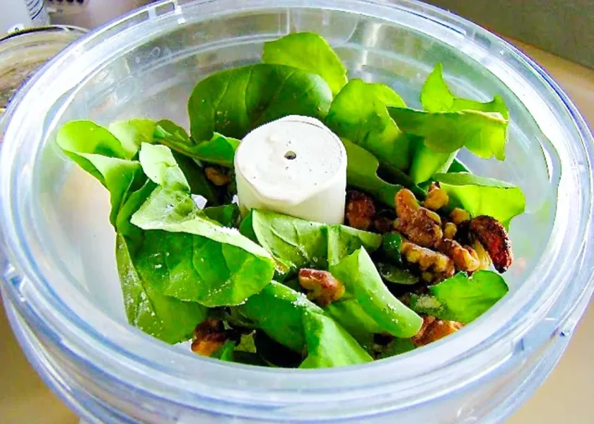 el tazón de un procesador de alimentos con rúcula y nueces para hacer pesto.