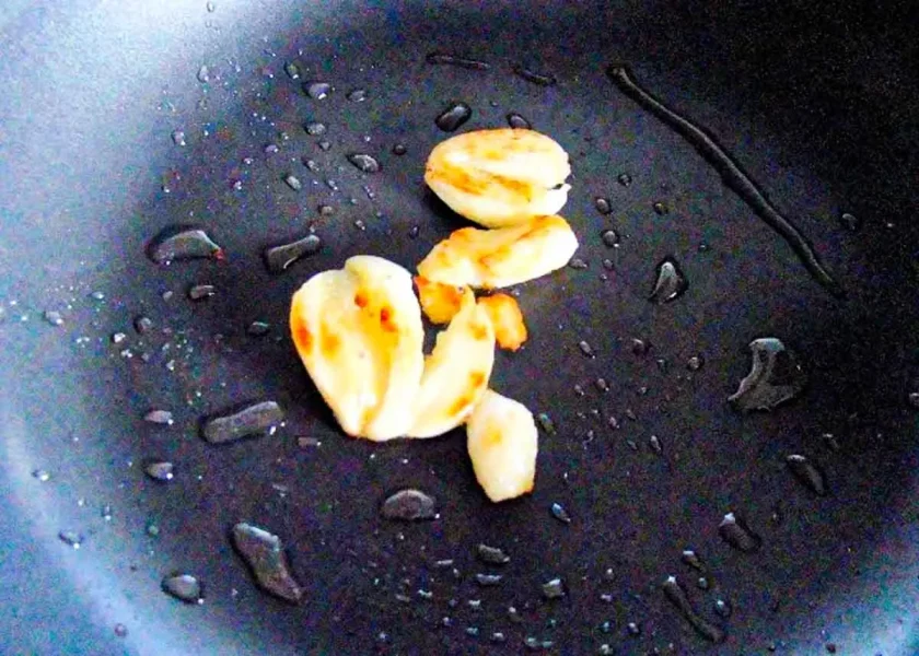 Smashed garlic cloves on a pan with drops of olive oil.