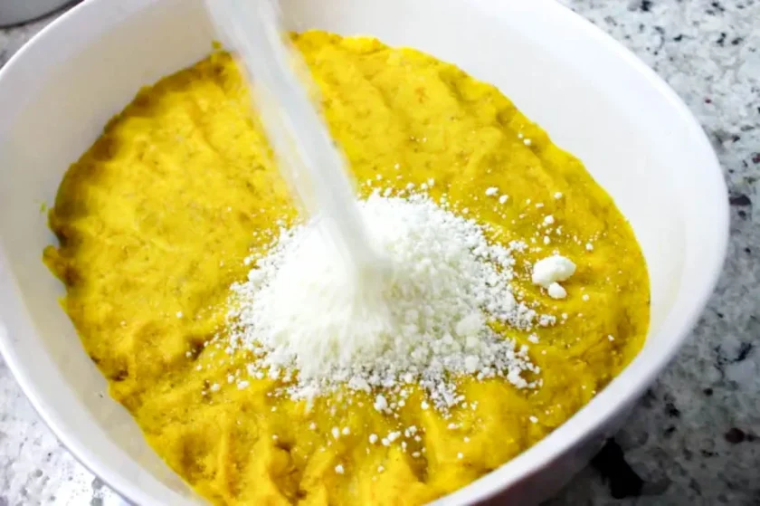 un poco de queso blanco rallado cae sobre un tazón con masa para hacer arepas de plåtano