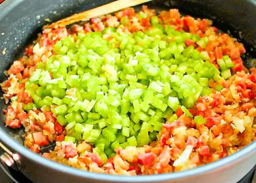 una sarten profunda con un sofrito de cebollas con cubitos de jaón y apio, para hacer sopa de arvejas con jamón.