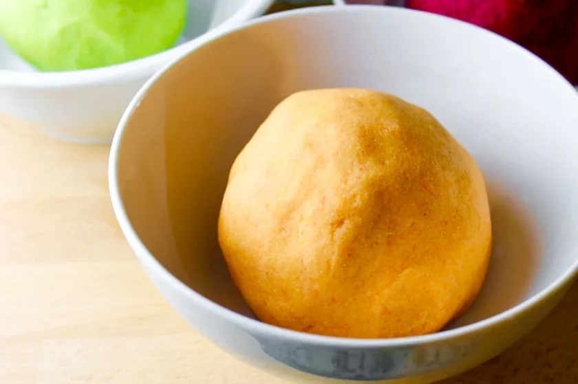 a white bowl with a ball of carrot arepa dough.