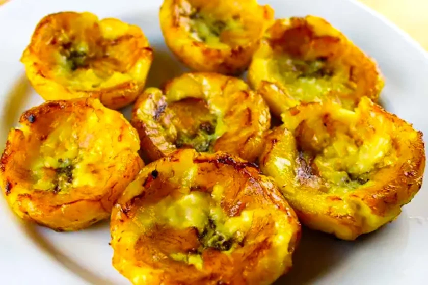 A white plate with eight fried yellow plantain cups filled with melted cheese and golden edges.