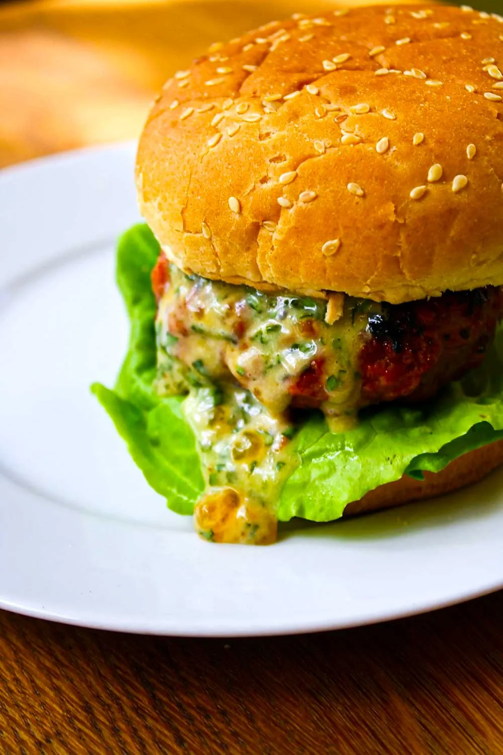 Una hamburguesa con lechuga y un pan con semillas de sésamo, con una hamburguesa cubierta de salsa de queso fundido, en un plato blanco.