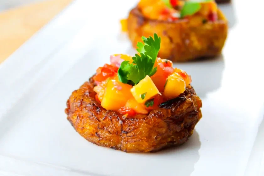 A fried ripe plantain cup filled with mango ceviche and a cilantro leaf, served on a white plate.