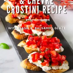 Sliced toasted bread topped with goat cheese, chopped strawberries, basil, and balsamic glaze, arranged on a black serving tray. Text reads: "Strawberry & Chevre Crostini Recipe.
