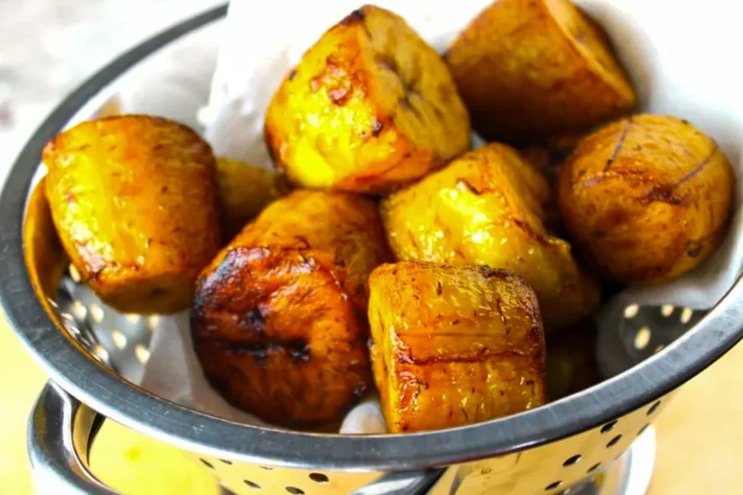 Golden fried plantain pieces piled in a metal colander lined with paper towels.
