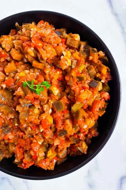 Un cuenco de eatatouilles hecho de verduras finamente picada con tomates, berenjenas y pimientos, adornado con un ramito de hierbas frescas, perfecto para quien busque una auténtica Receta de pisto llena de sabor y tradición.