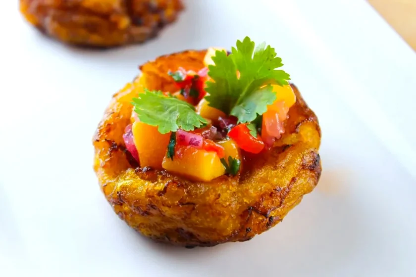 Una pequeña cesta redonda de plátano frito rellena de salsa de mango en dados y adornada con cilantro fresco en un plato blanco.