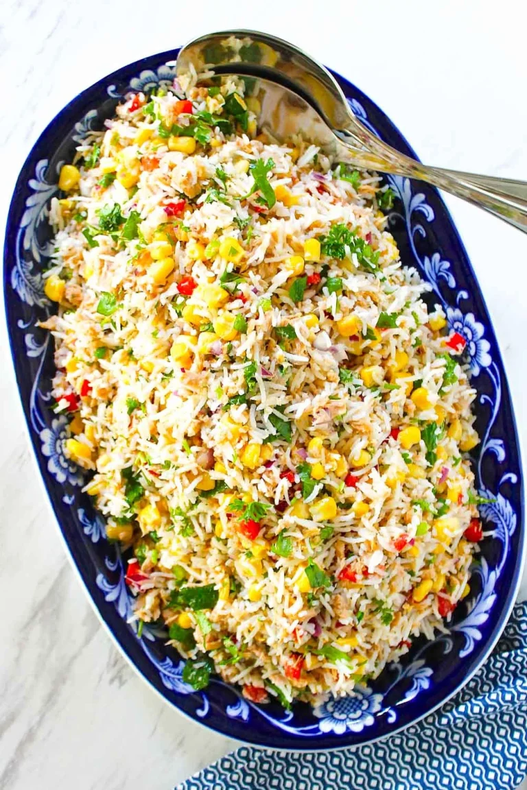 Plato ovalado de color azul relleno de ensalada de arroz con maíz, hierbas picadas y verduras rojas y verdes cortadas en dados, con una cuchara para servir al lado.
