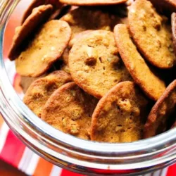 Un tarro de cristal lleno de galletas de jengibre con nueces pecanas, descansa sobre un paño a rayas, visto desde arriba.