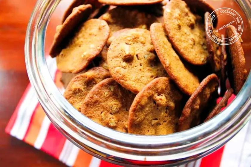 A glass jar filled with double ginger snaps with pecans and white pepper rests on a striped kitchen towel, seen from above.
