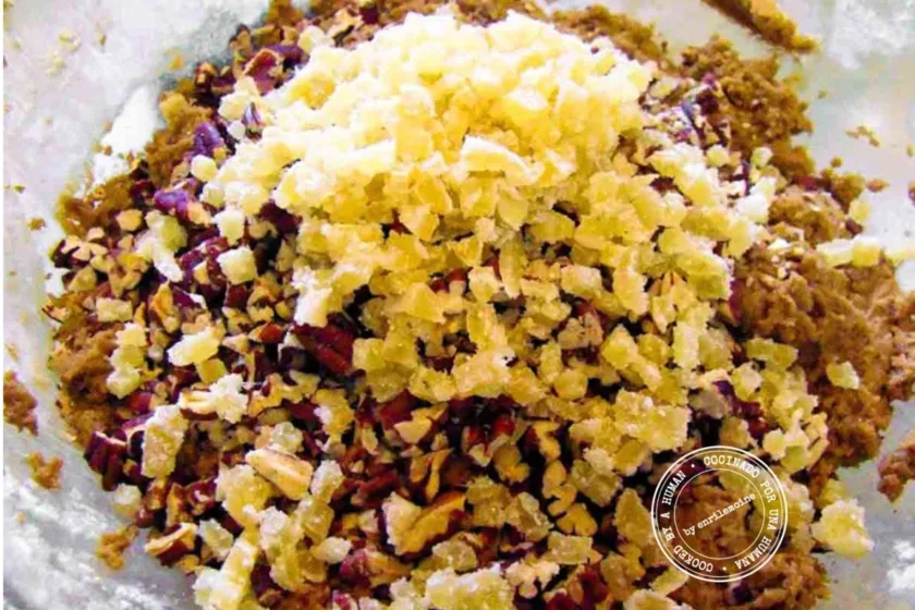 A close-up of chopped crystallized ginger and pecans on top of cookie dough in a bowl.