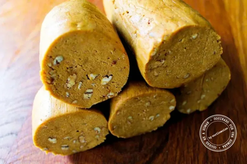 Six logs of double ginger snap dough with visible pecan pieces, stacked on a wooden surface.