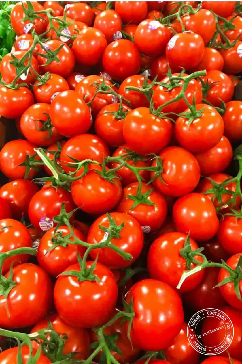 Un montón de tomates rojos maduros con tallos verdes, apilados muy juntos.