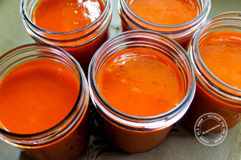 Cinco tarros de cristal llenos de salsa de tomate de un color naranja intenso están colocados muy juntos sobre una superficie plana.