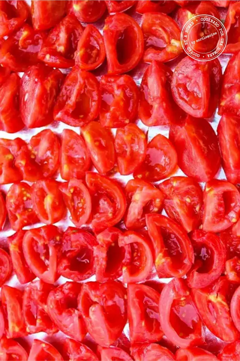 Varias filas de tomates rojos cortados por la mitad y en cuartos están dispuestas sobre una superficie plana, dejando a la vista su pulpa y sus semillas.