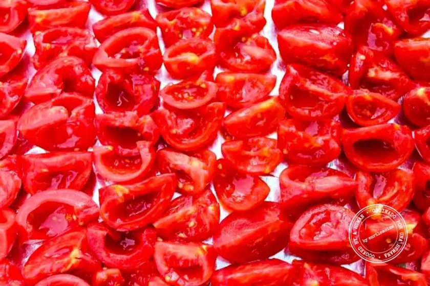 Rows of quartered red tomatoes arranged close together on a foil-lined baking sheet, ready to be roasted.