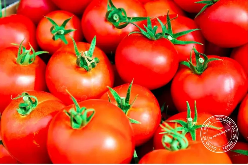 Un primer plano de varios tomates rojos maduros con tallos verdes, apilados unos sobre otros.
