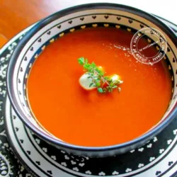 Un plato de sopa de tomate con una cucharada de nata y decorado con hierbas frescas, servido en un plato estampado con una cuchara.