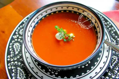 Un plato de sopa de tomate con una cucharada de nata y decorado con hierbas frescas, servido en un plato estampado con una cuchara.