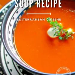 Un cuenco de sopa de tomate asado adornado con hierbas, servido en un plato estampado. El texto superpuesto dice: «Receta de sopa de tomate asado, cocina mediterránea».