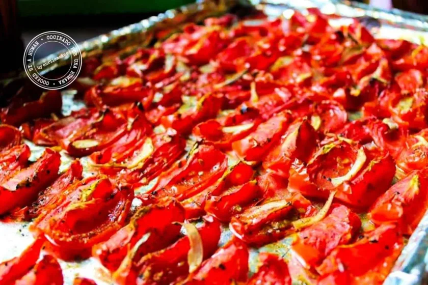 Rows of quartered roasted tomatoes on a foil-lined baking sheet, seasoned with herbs, olive oil, and garlic.