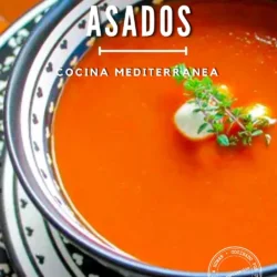 Un cuenco de sopa de tomate asado adornado con nata y hierbas, servido en un plato estampado. El texto de la imagen dice: «Sopa de tomates asados, cocina mediterránea».