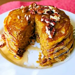 A stack of pancakes topped with pecans and syrup on a white plate, with a wedge cut out.