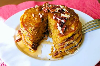 A stack of pancakes topped with pecans and syrup on a white plate, with a wedge cut out.
