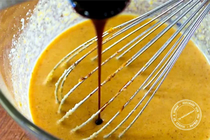 Dark molasses being poured into a bowl of pumpkin pancake batter as it is mixed with a wire whisk.