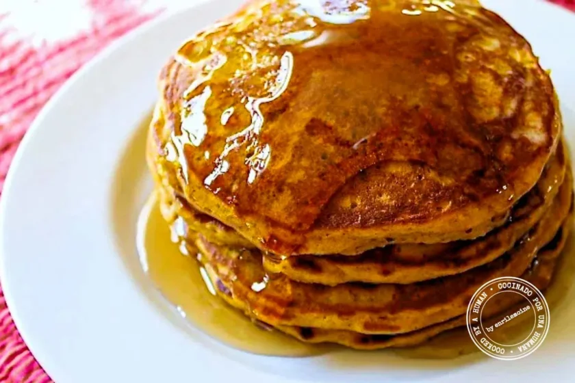 A stack of pancakes on a white plate covered in syrup.