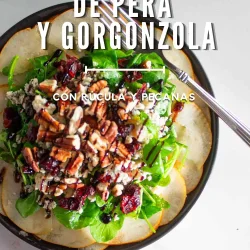 Una ensalada de rúcula, gorgonzola, nueces pecanas y arándanos rojos secos servida sobre peras cortadas en finas rodajas, con el texto: «Carpaccio de pera y gorgonzola con rúcula y nueces pecanas».