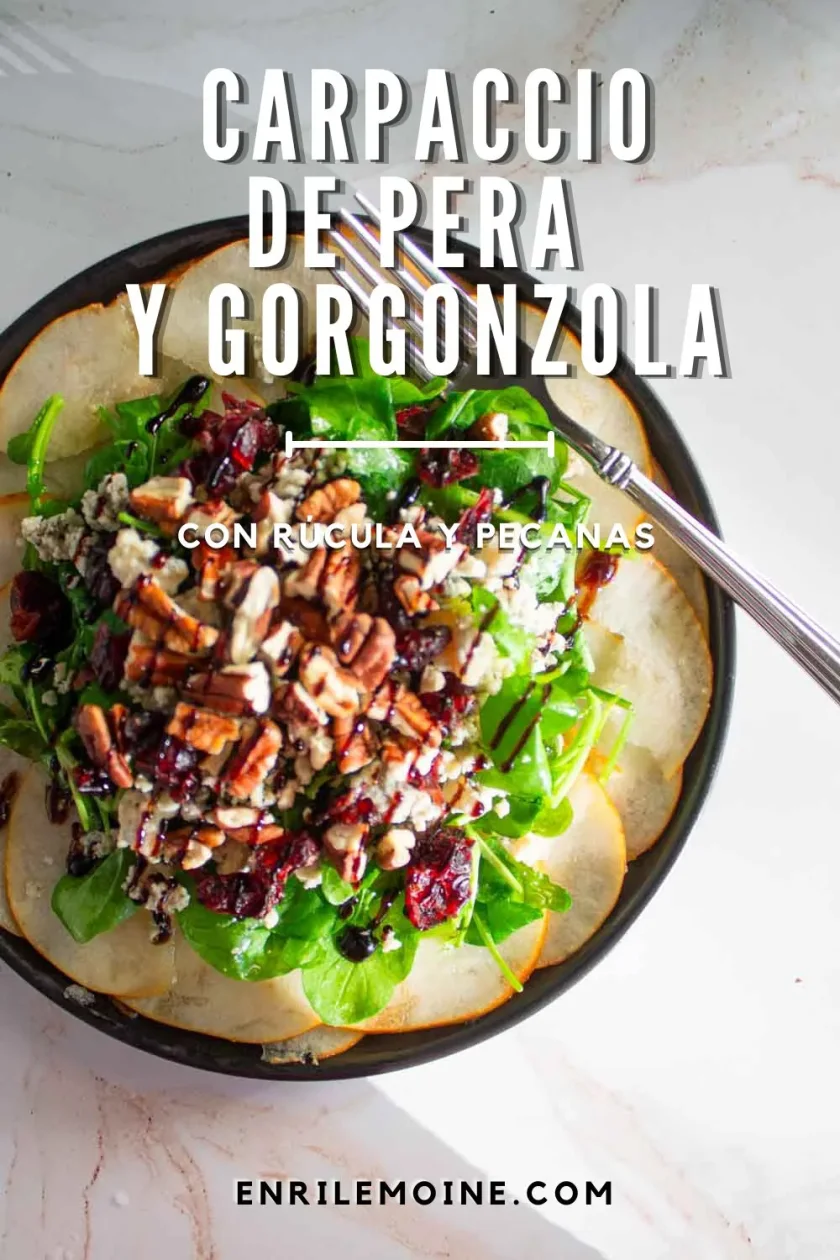 Una ensalada de rúcula, gorgonzola, nueces pecanas y arándanos rojos secos servida sobre peras cortadas en finas rodajas, con el texto: «Carpaccio de pera y gorgonzola con rúcula y nueces pecanas».